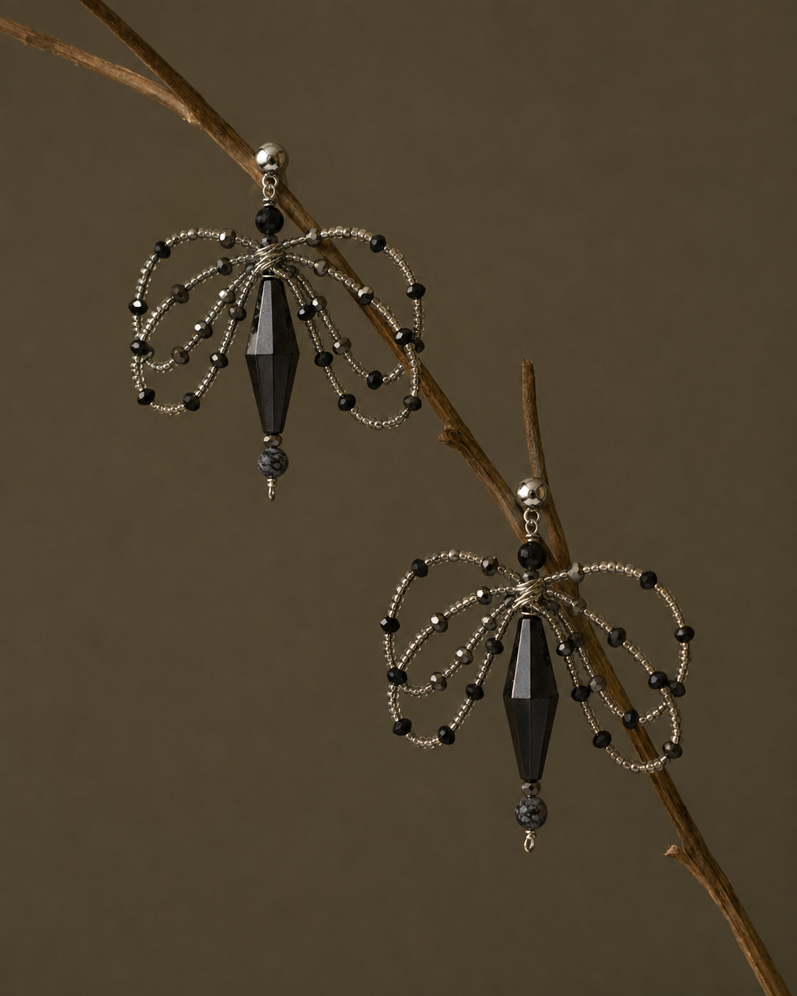 Pair of black and silver beaded Gardenia earrings hanging from a bare branch